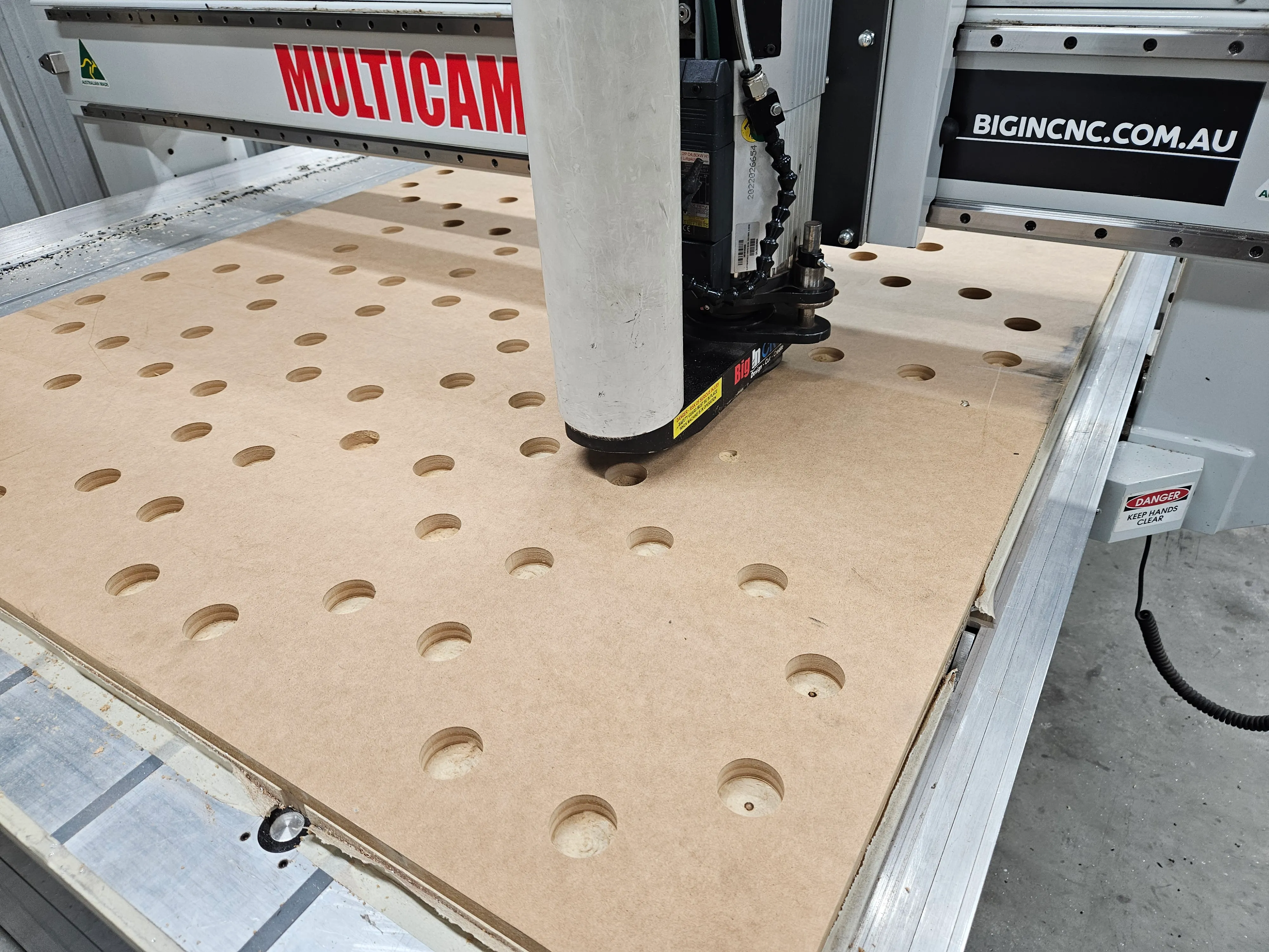 Closer view of the MDF panel on the Multicam bed during the hole-drilling pass