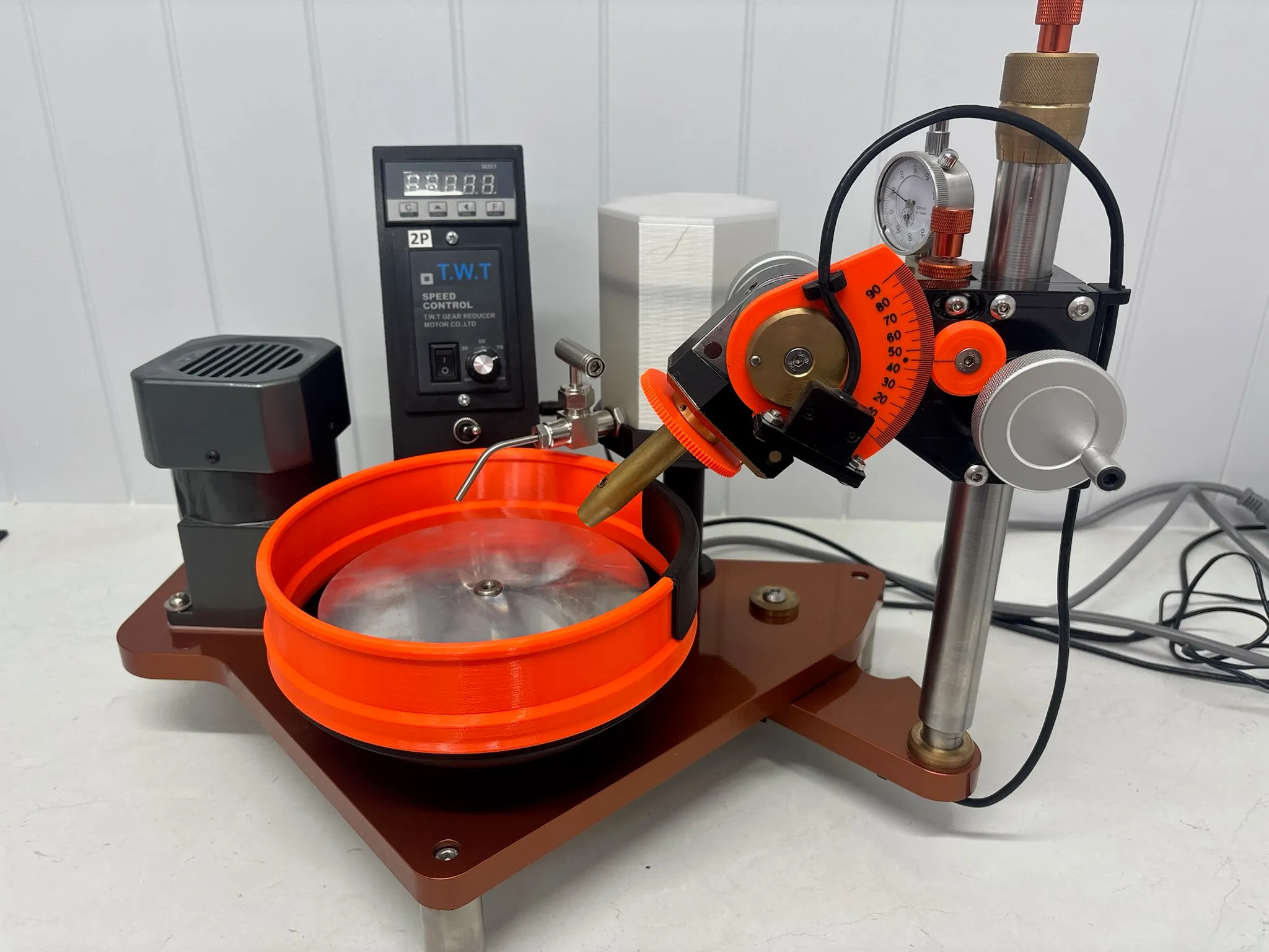 Assembled gemstone lapping machine — bronze base plate, vertical post with dial gauge, orange polishing bowl, angle gauge and speed-controlled drive motor